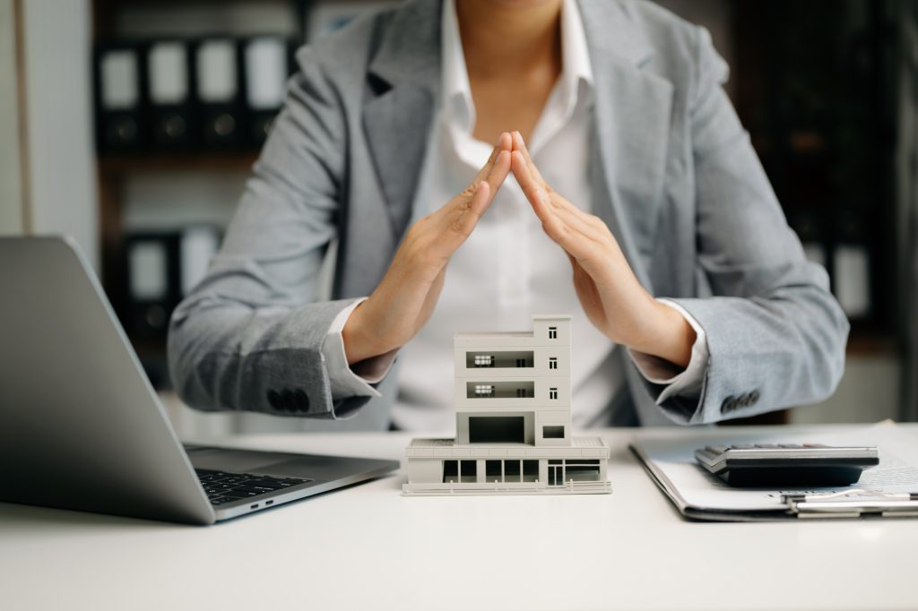 Female real estate agent is use hands to protect red roof for the concept of real estate investment